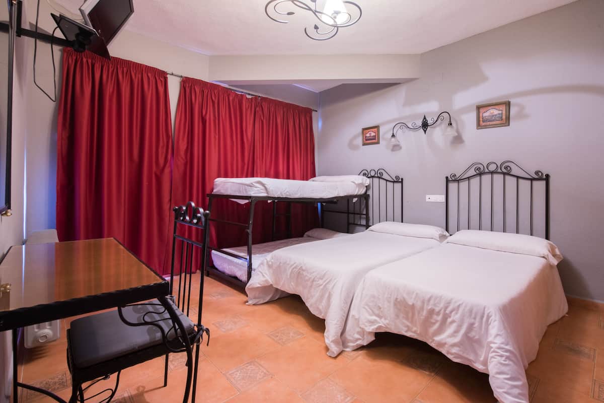 A room with a bunk bed, a single bed, a table with chairs, and a red curtain.