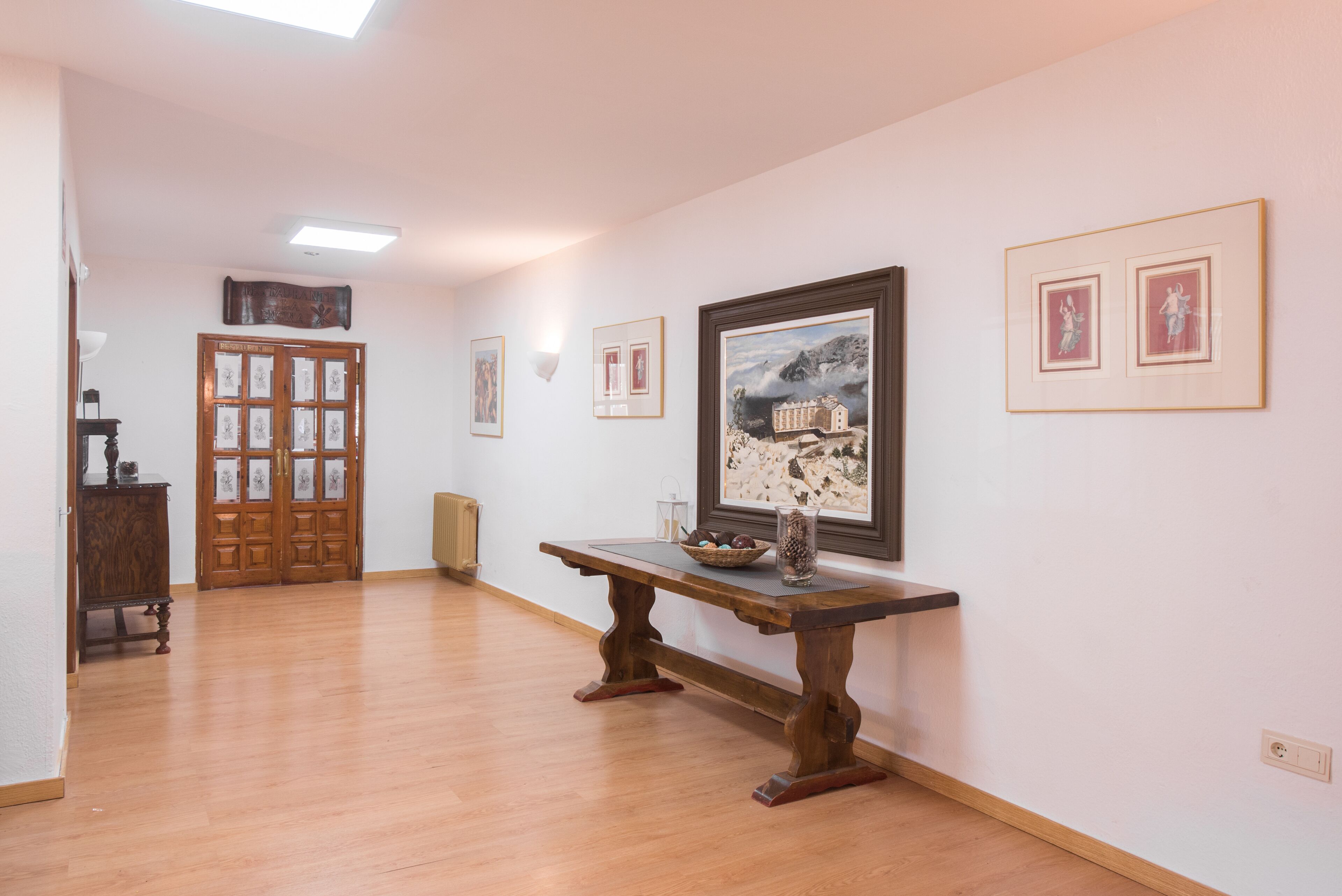 A hallway with wooden flooring, a wooden bench, framed artwork on the walls, and a door with glass panels.
