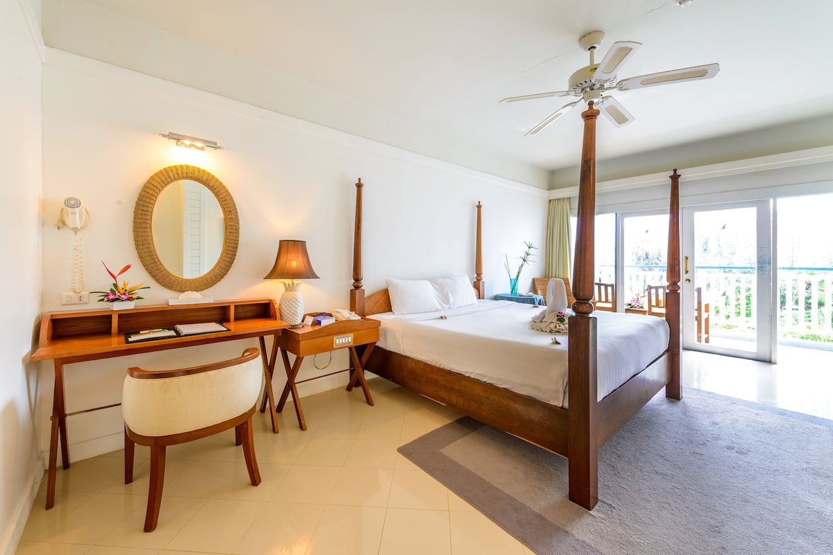 Habitación de hotel con cama con dosel, un escritorio con silla, tocador con espejo y balcón con vistas.
