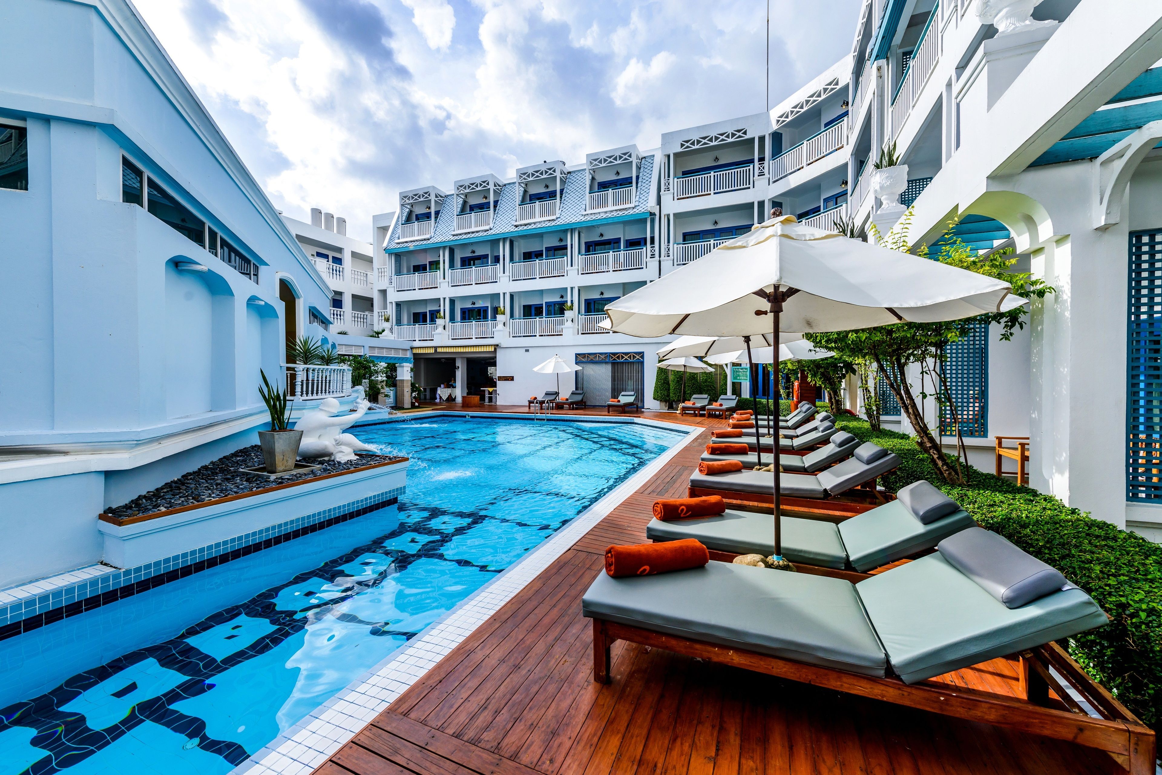 Un espace piscine doté de chaises longues et de parasols, entouré d’un immeuble à plusieurs étages avec des balcons.