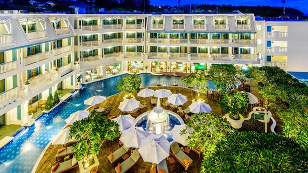 A multi-story hotel with a central swimming pool, outdoor seating areas, and lush greenery. - Andaman Seaview Hotel (Karon)