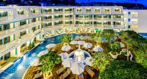 Un hotel de varios pisos con piscina central, zonas de estar al aire libre y abundante vegetación.