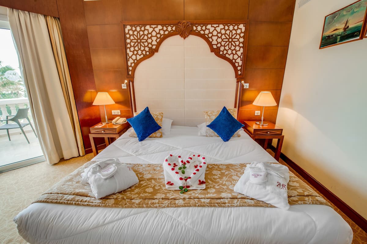 Une chambre d’hôtel avec un grand lit, deux tables de chevet, une tête de lit décorative et une vue sur l’extérieur.