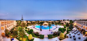 A resort with a central pool, multiple dining areas, and a view of the sea.