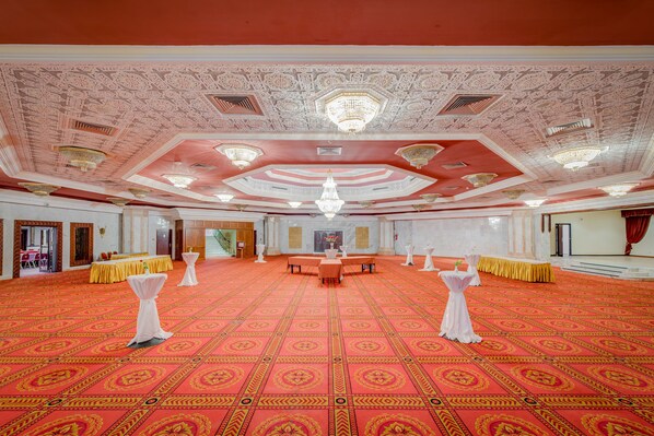 A large hall with a patterned red carpet, white columns, and chandeliers.