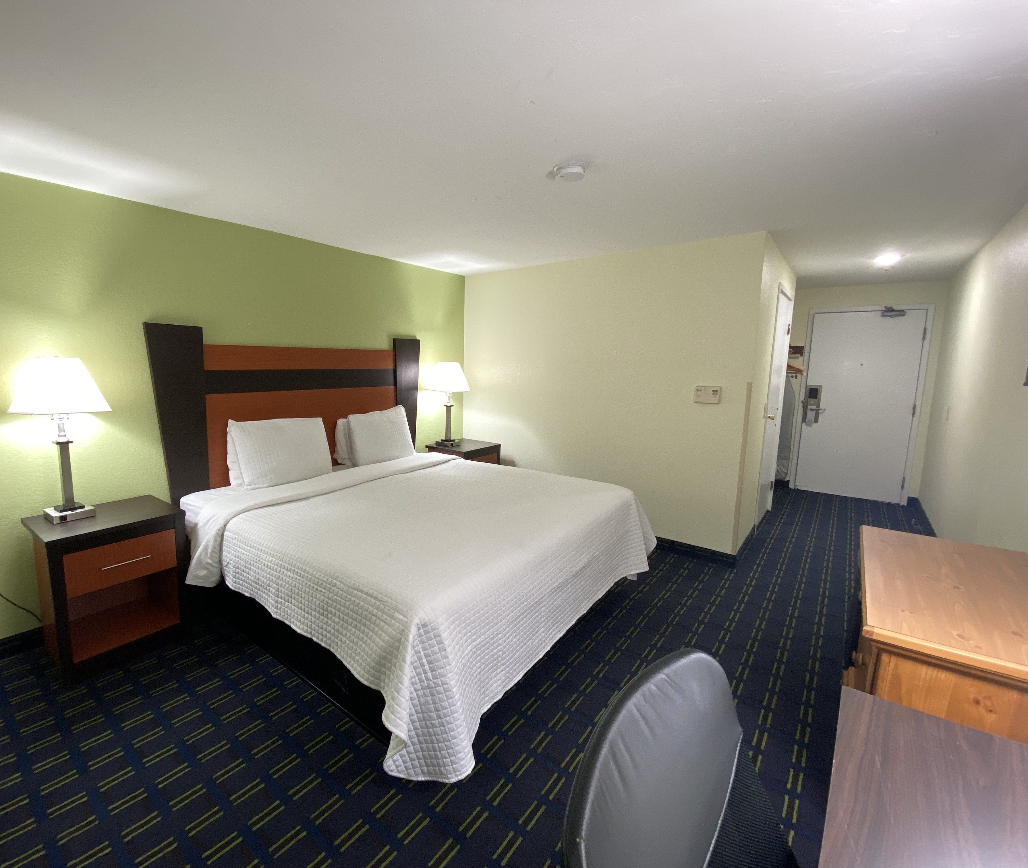 A hotel room with a bed, two bedside tables with lamps, a desk, and a chair.