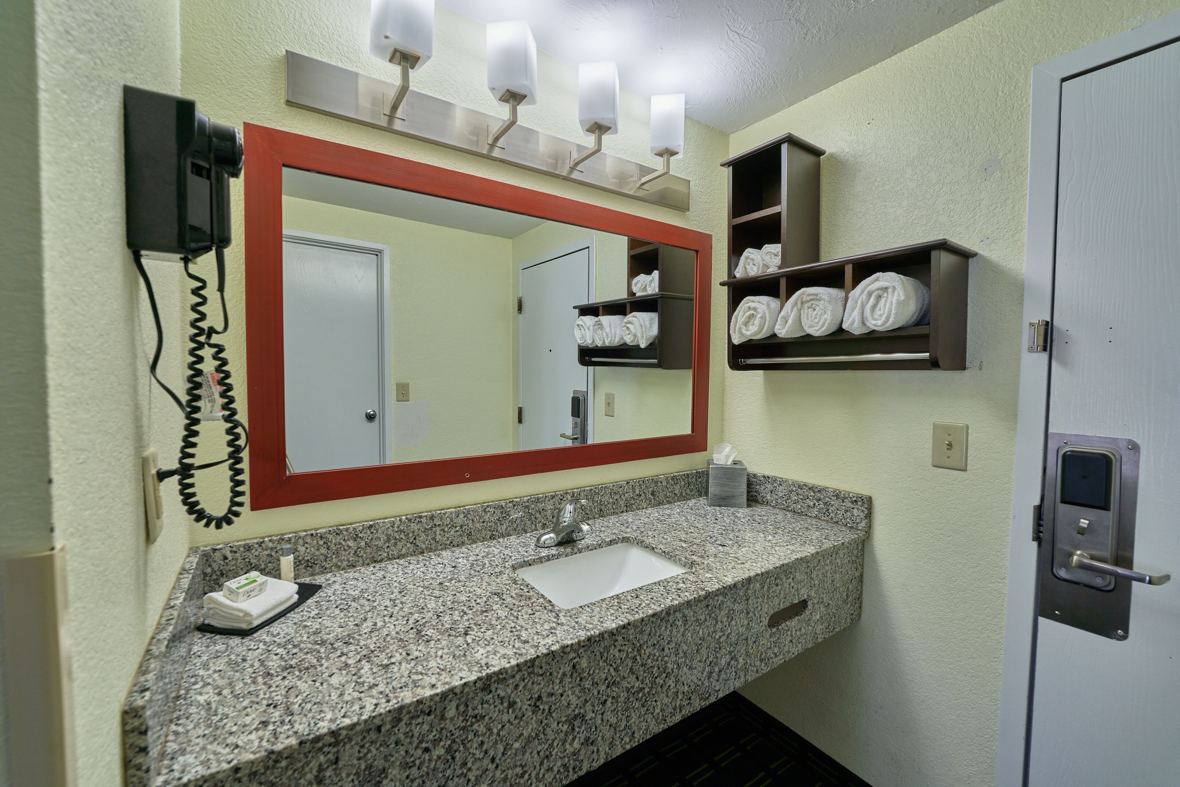A bathroom with a granite sink, a mirror with a red frame, a towel rack, and a telephone.