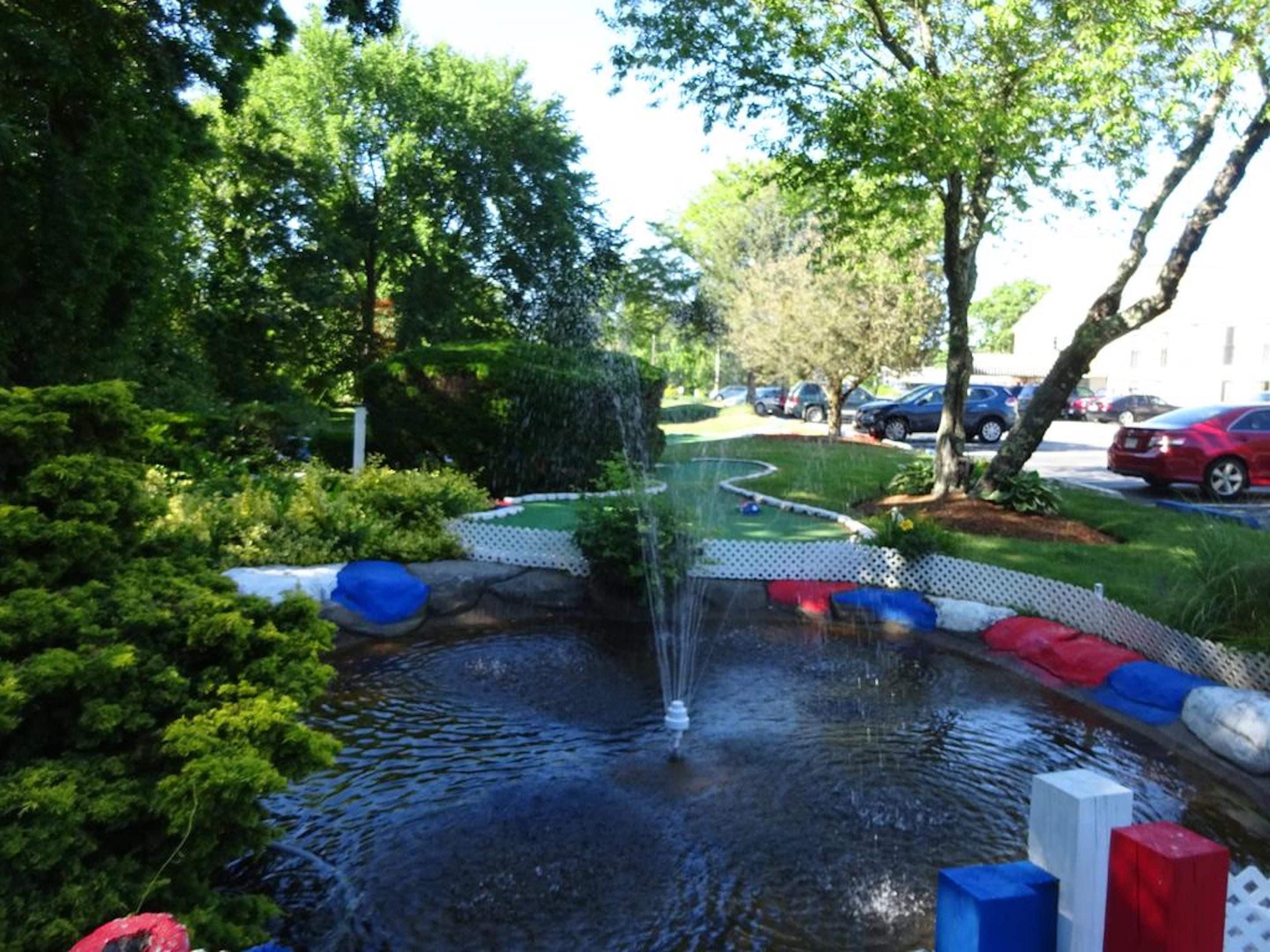 Een aangelegd gebied met een waterpartij, omringd door bomen en een pad.