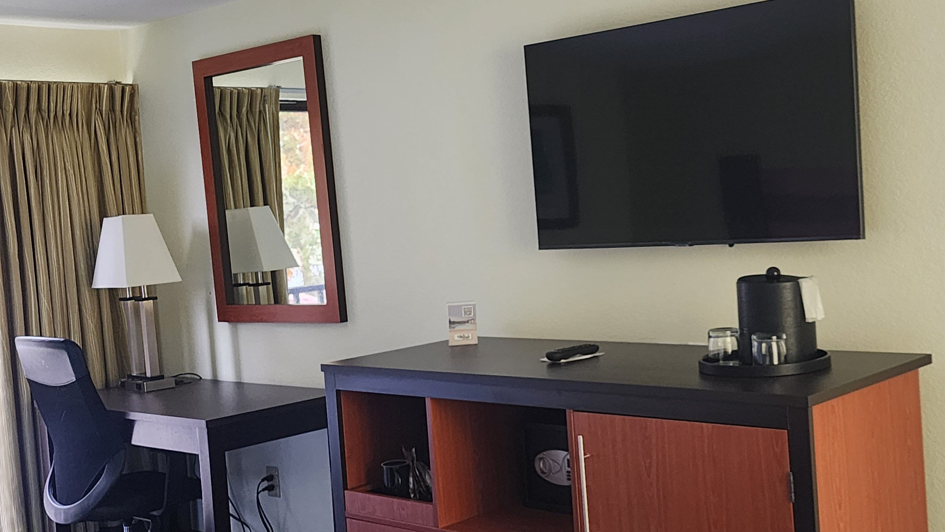 A hotel room with a desk, chair, television, and a coffee maker.