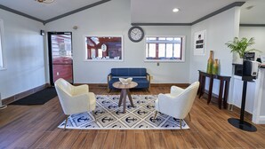 Un hall d’entrée moderne avec un canapé bleu, deux fauteuils, une table ronde et une horloge au mur.