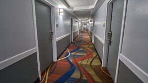 Ein langer, schmaler Hotelkorridor mit Türen an beiden Seiten, einem gemusterten Teppich und wandmontierten Leuchten.