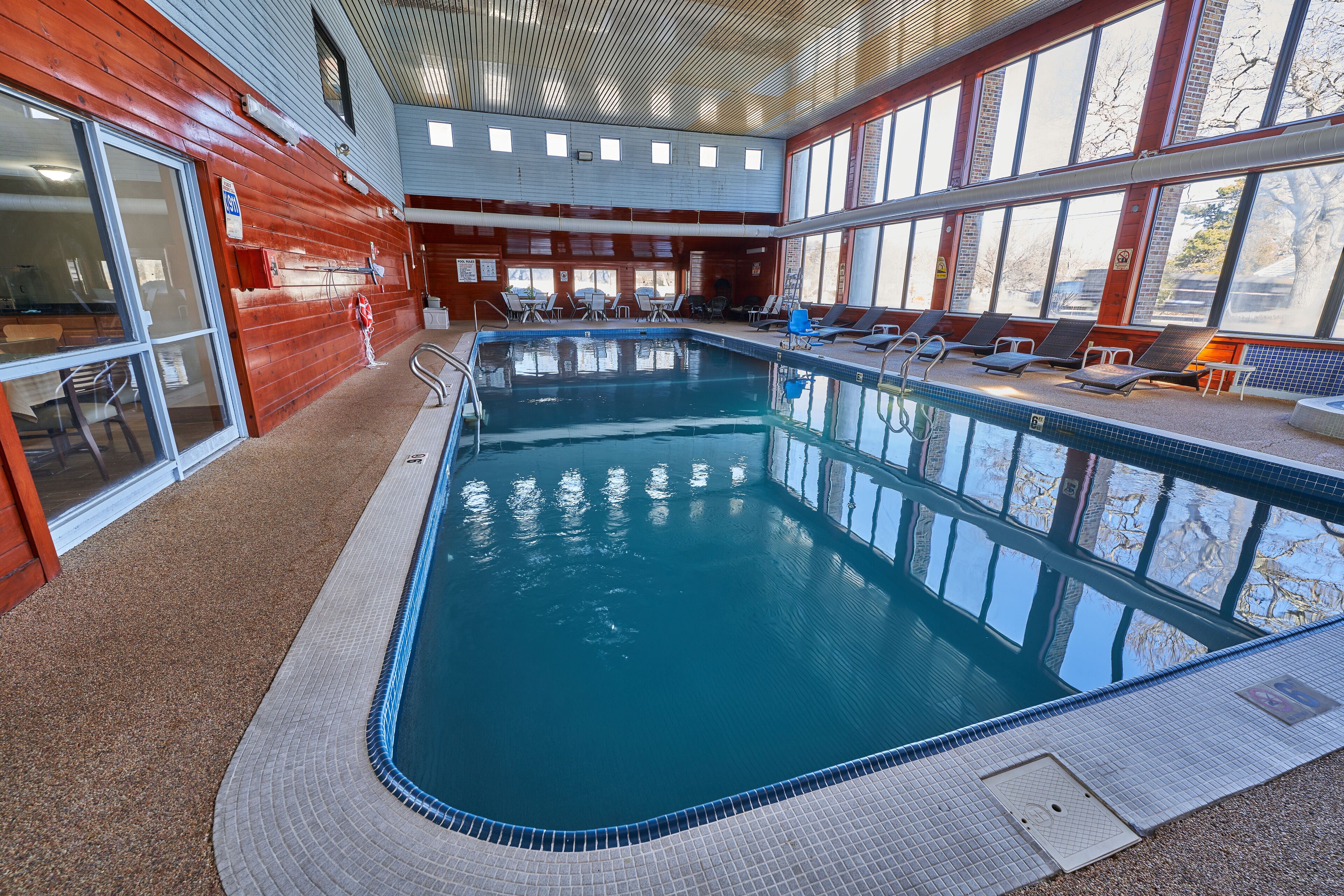 An indoor swimming pool with clear blue water, surrounded by lounge chairs and a tiled deck.
