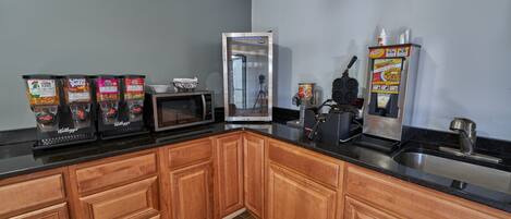 A kitchen with wooden cabinets, a black countertop, a microwave, a coffee maker, and a cereal dispenser.