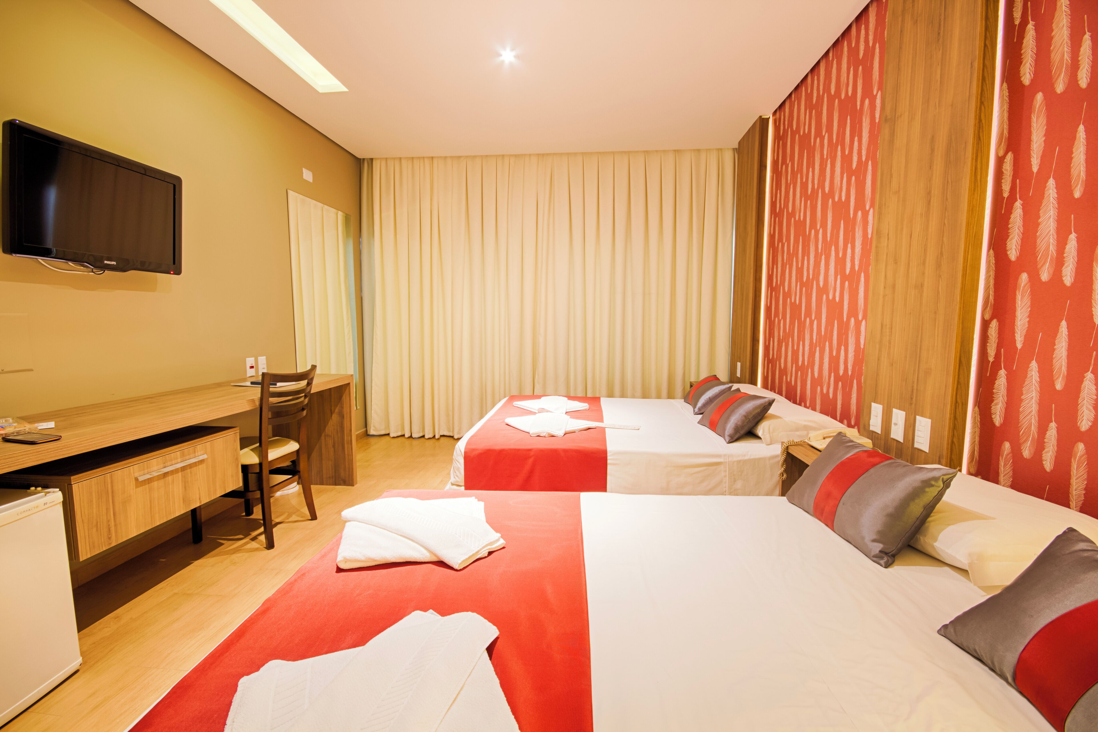 A hotel room with two beds, a desk, a chair, and a television.