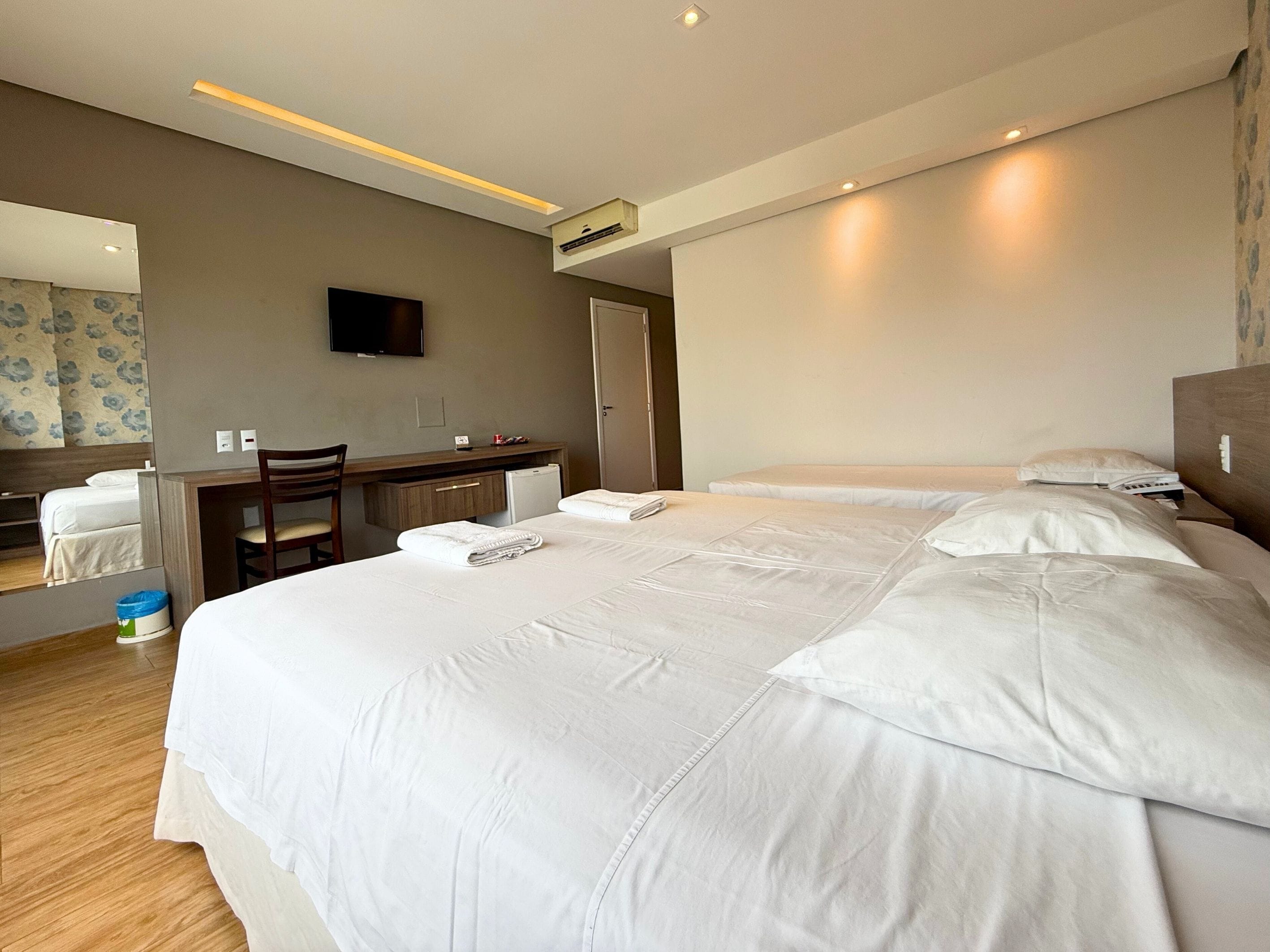 Une chambre d’hôtel avec un grand lit, un bureau, une chaise, un téléviseur à écran plat et un petit réfrigérateur.