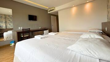Une chambre d’hôtel avec un grand lit, un bureau, une chaise, un téléviseur à écran plat et un petit réfrigérateur.