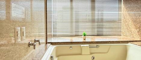 Un baño moderno con una bañera grande, una pequeña planta en maceta en el alféizar de la ventana y una pared con textura.