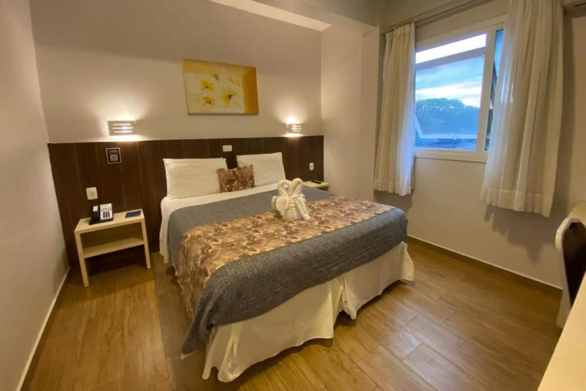 Una habitación de hotel con cama, mesita de noche y una ventana con cortinas.