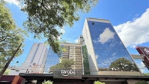 Un hotel con fachada de vidrio moderna, con un letrero que dice 'tarova hotel' a la vista y un coche rojo estacionado en la entrada.