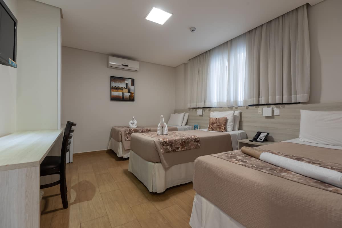 Habitación de hotel con dos camas, un escritorio y una silla. Cuenta con ventana con cortinas, unidad de aire acondicionado y un cuadro en la pared.