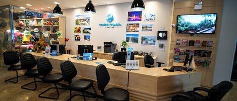 A reception desk with black chairs, a computer, and a TV on the wall.