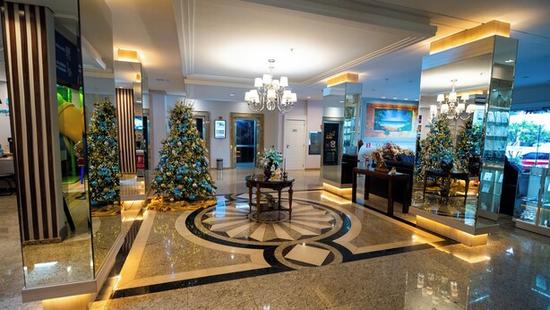 Un vestíbulo con piso de mármol pulido, árboles de Navidad y una lámpara de araña central.