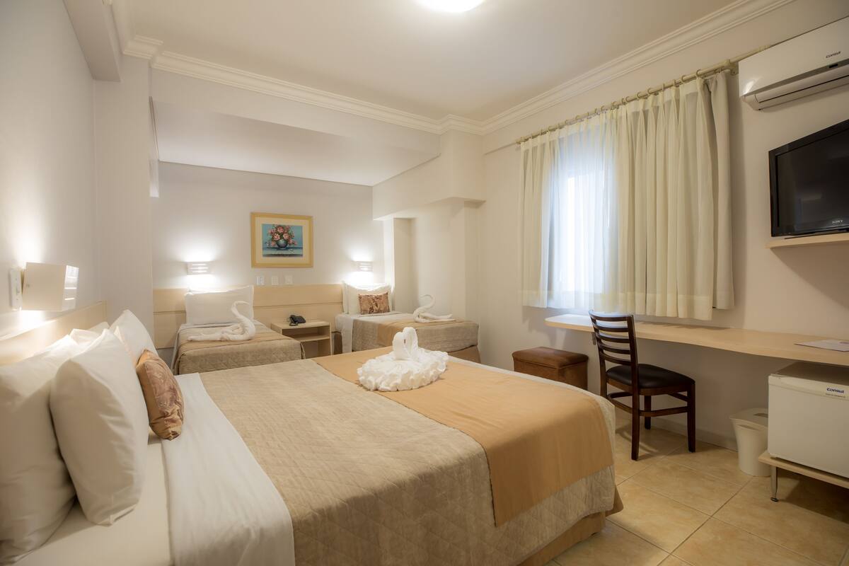 Una habitación de hotel con dos camas, un escritorio, una silla, un televisor y un cuadro en la pared.
