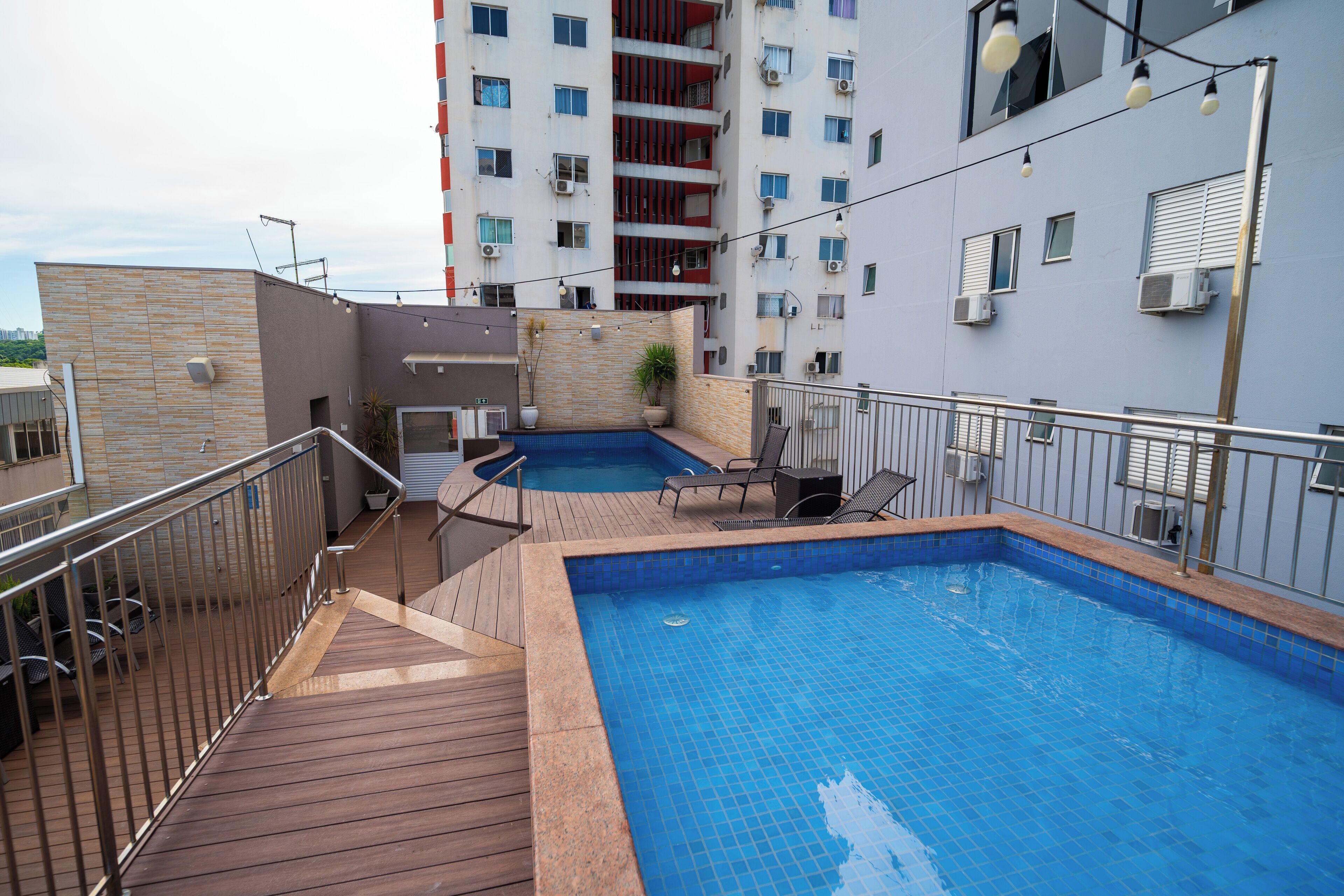 A rooftop swimming pool with two separate sections, surrounded by a wooden deck and metal railings.