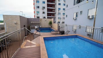 A rooftop swimming pool with two separate sections, surrounded by a wooden deck and metal railings.
