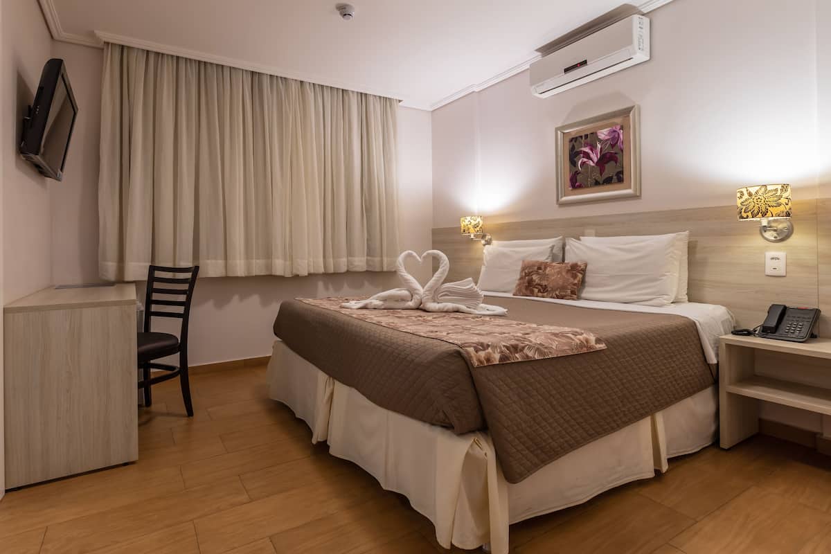 Una habitación de hotel con cama, mesita de noche, lámpara y televisor montado en la pared.