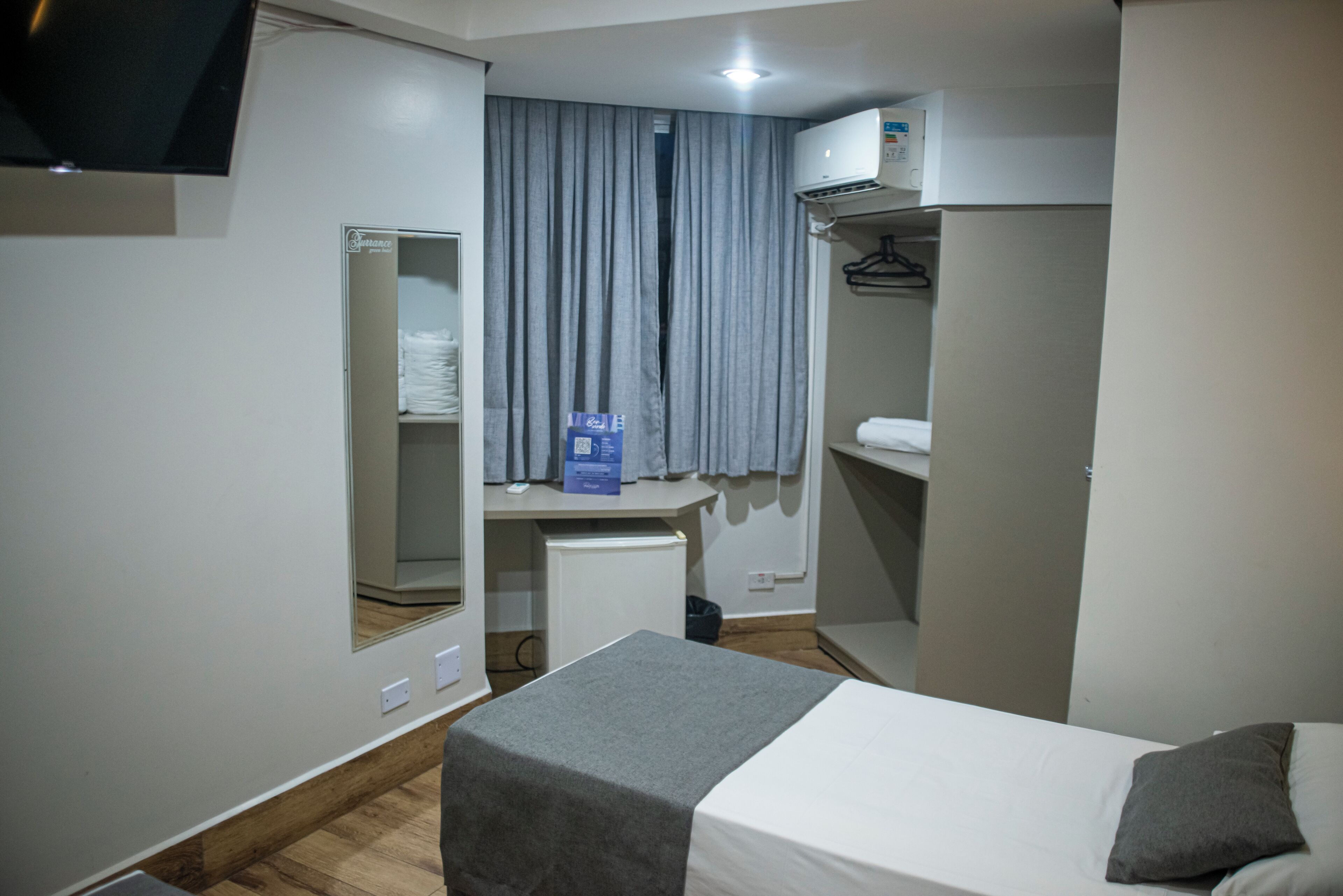 A hotel room with a bed, a desk, a wardrobe, and an air conditioning unit.