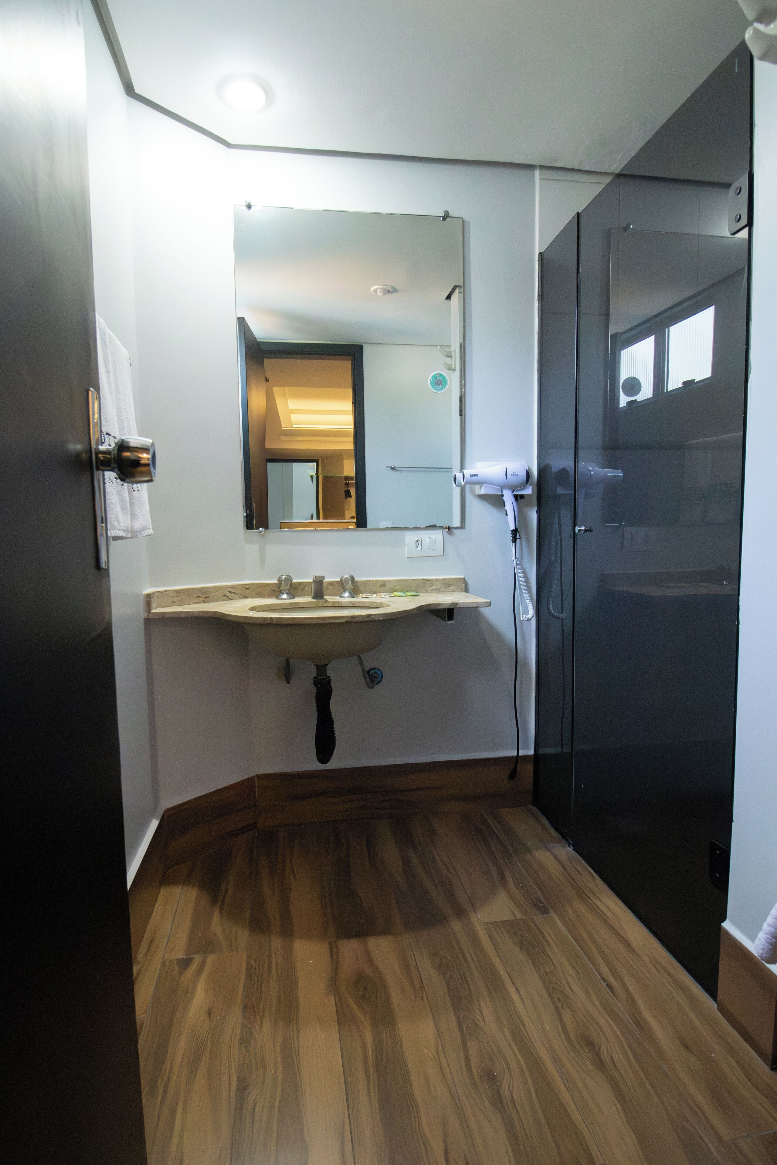 A bathroom with a wooden floor, a sink with a mirror above it, and a shower area.