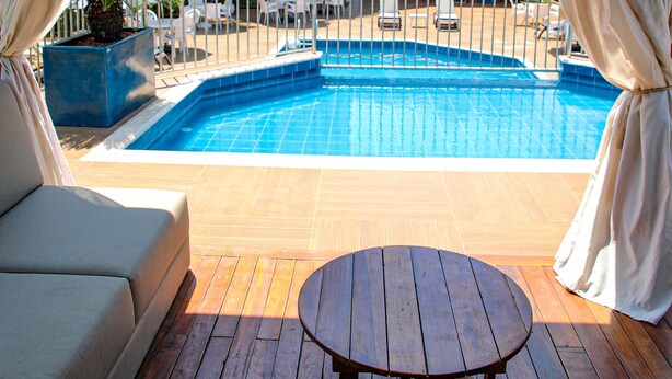 A poolside area with a wooden deck, a round table, and a sofa. - Hotel Portinari Centro (Foz do Iguaçu)