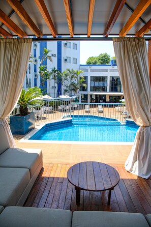 A poolside area with a wooden deck, a round table, and a sofa.