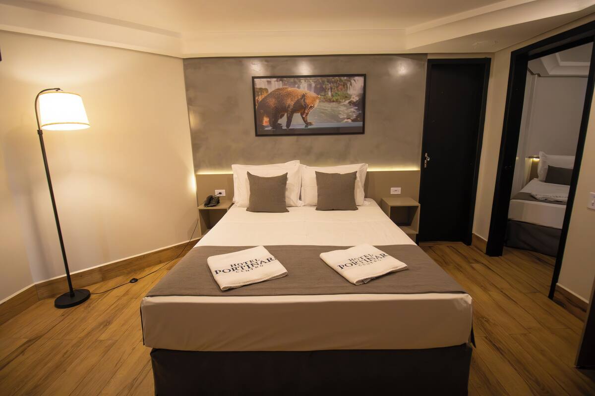 Een hotelkamer met een groot bed, twee kussens, een nachtkastje, een lamp en een schilderij van een beer aan de muur.