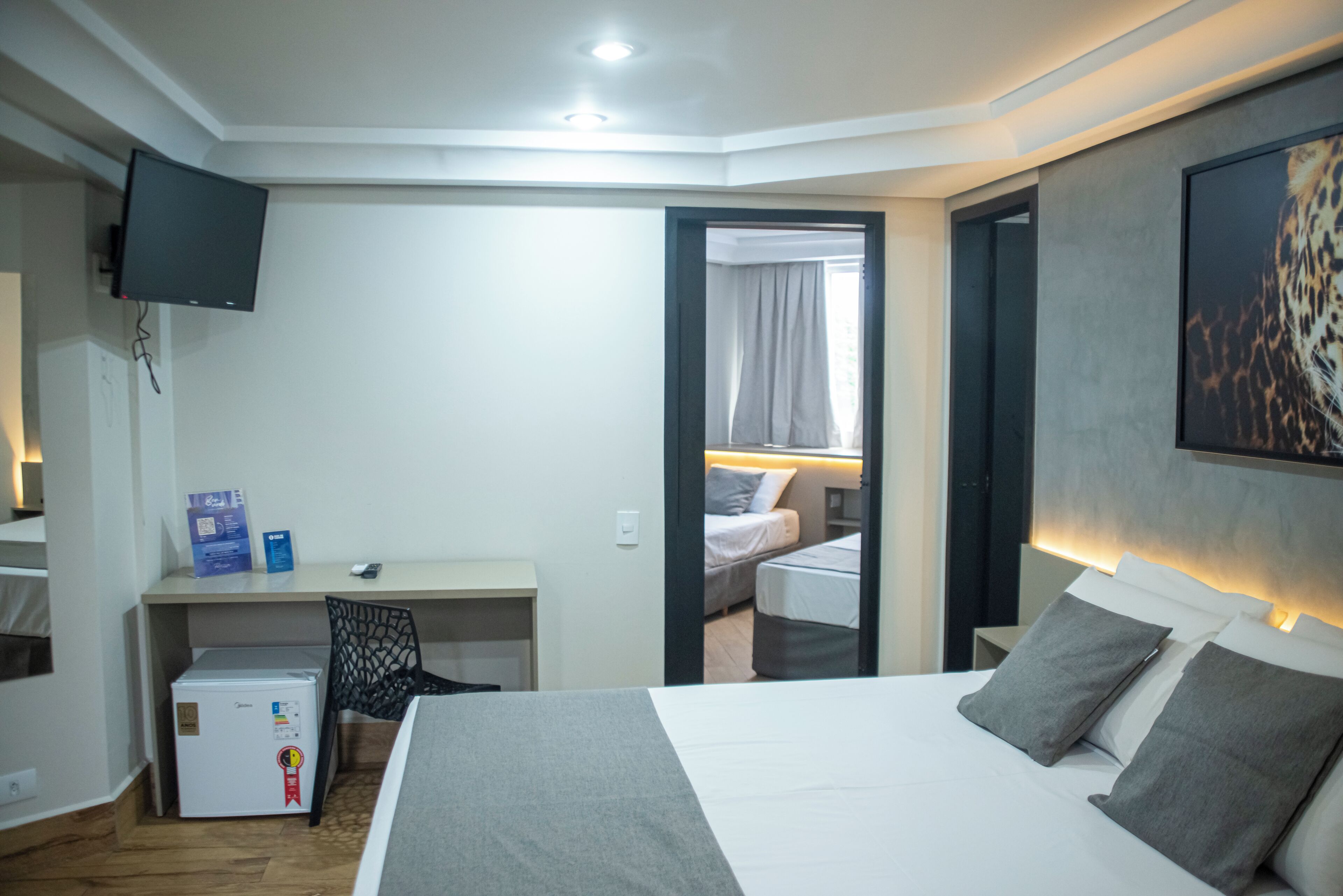 Une chambre d’hôtel équipée d’un lit, d’un bureau, d’une chaise, d’un téléviseur fixé au mur et d’un réfrigérateur.