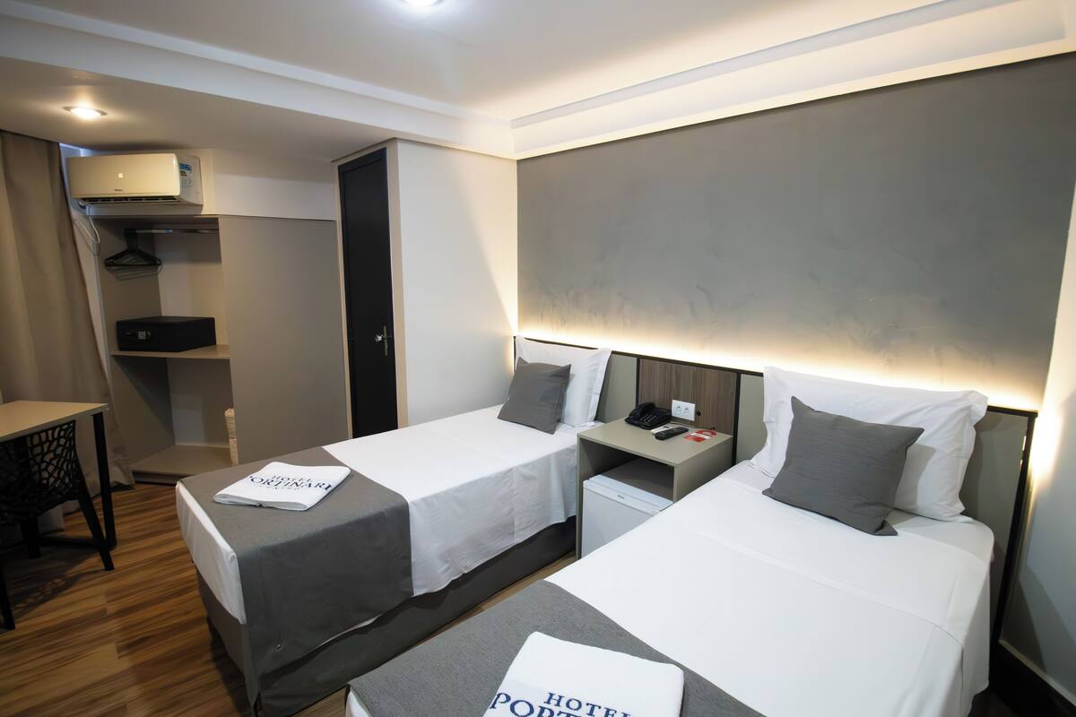 Hotelkamer met twee bedden, een bureau, een stoel, een kast en een klein bureau met telefoon en lamp.