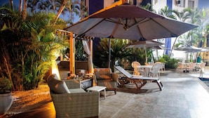 An outdoor patio area with wicker furniture, umbrellas, and a pool. - Hotel Portinari Centro (Foz do Iguaçu)