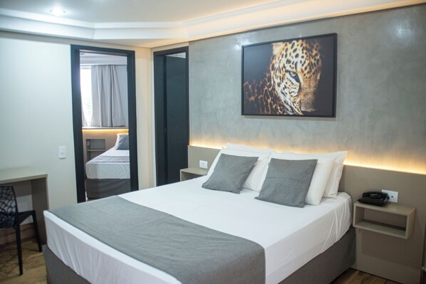 A modern hotel room with a large bed, bedside tables, a desk, and a mirror.