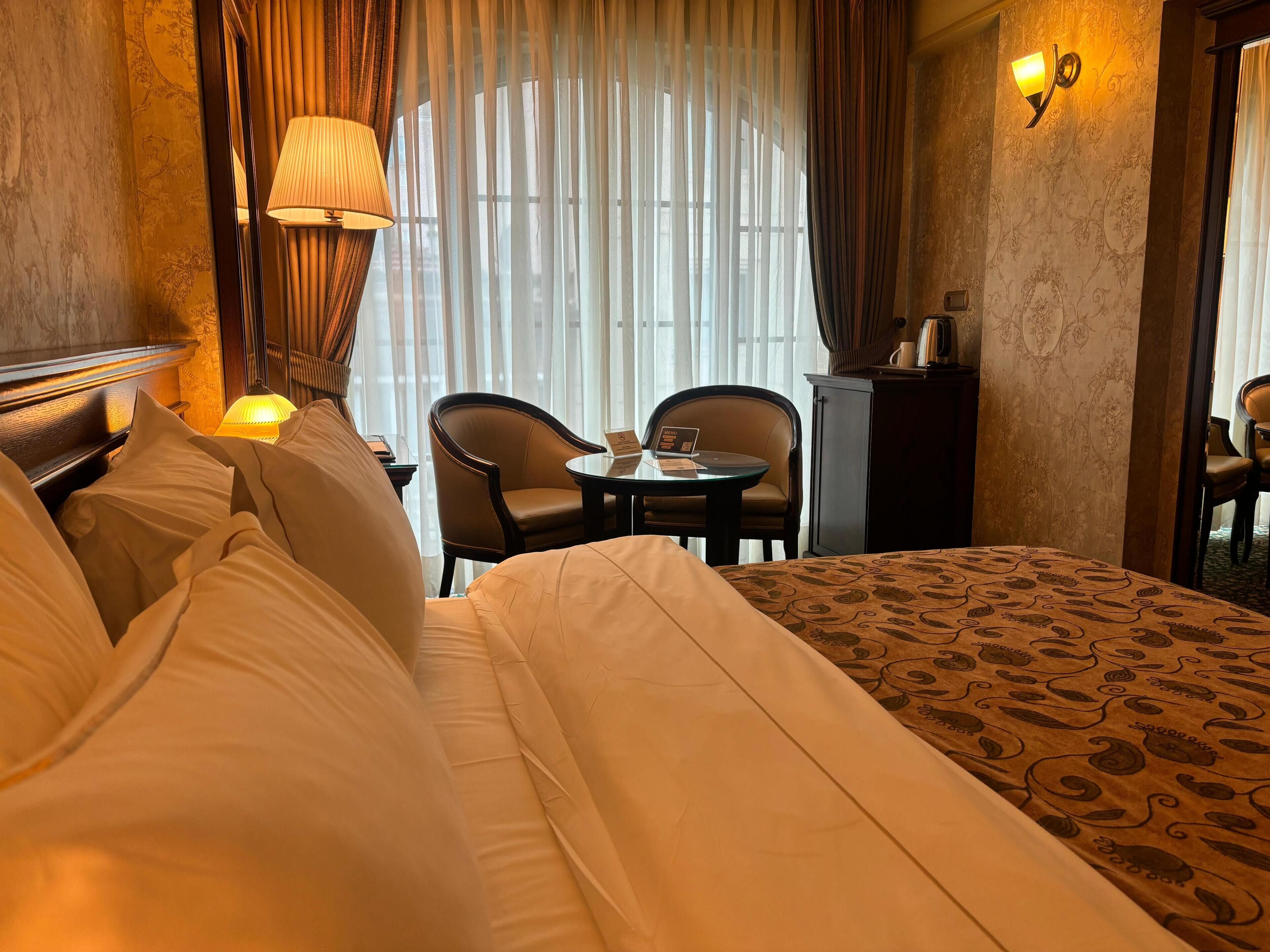 A hotel room with a bed, two chairs, a small table, a lamp, and a cabinet.