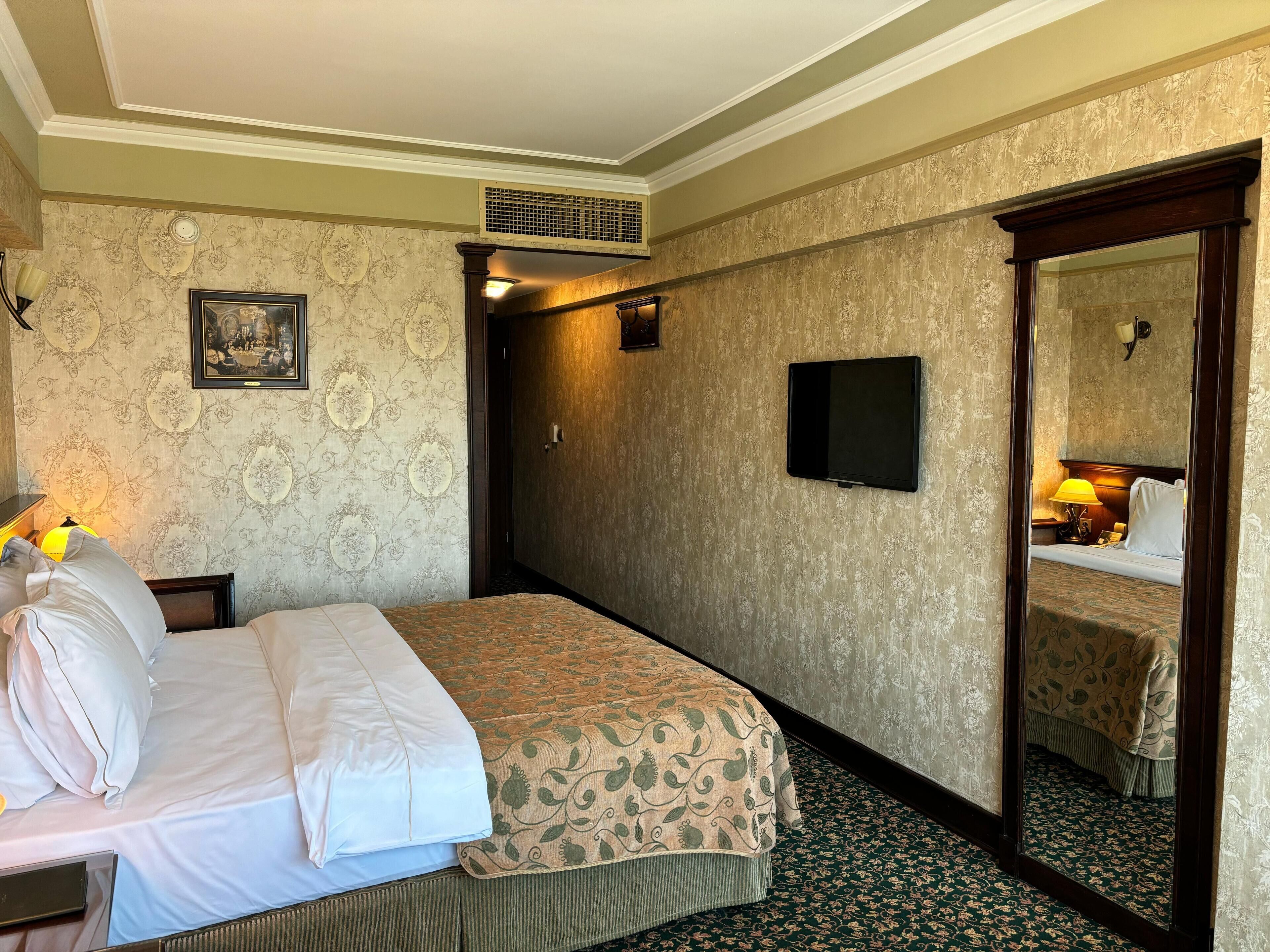 A hotel room with a bed, a television, a mirror, and a door leading to a bathroom.
