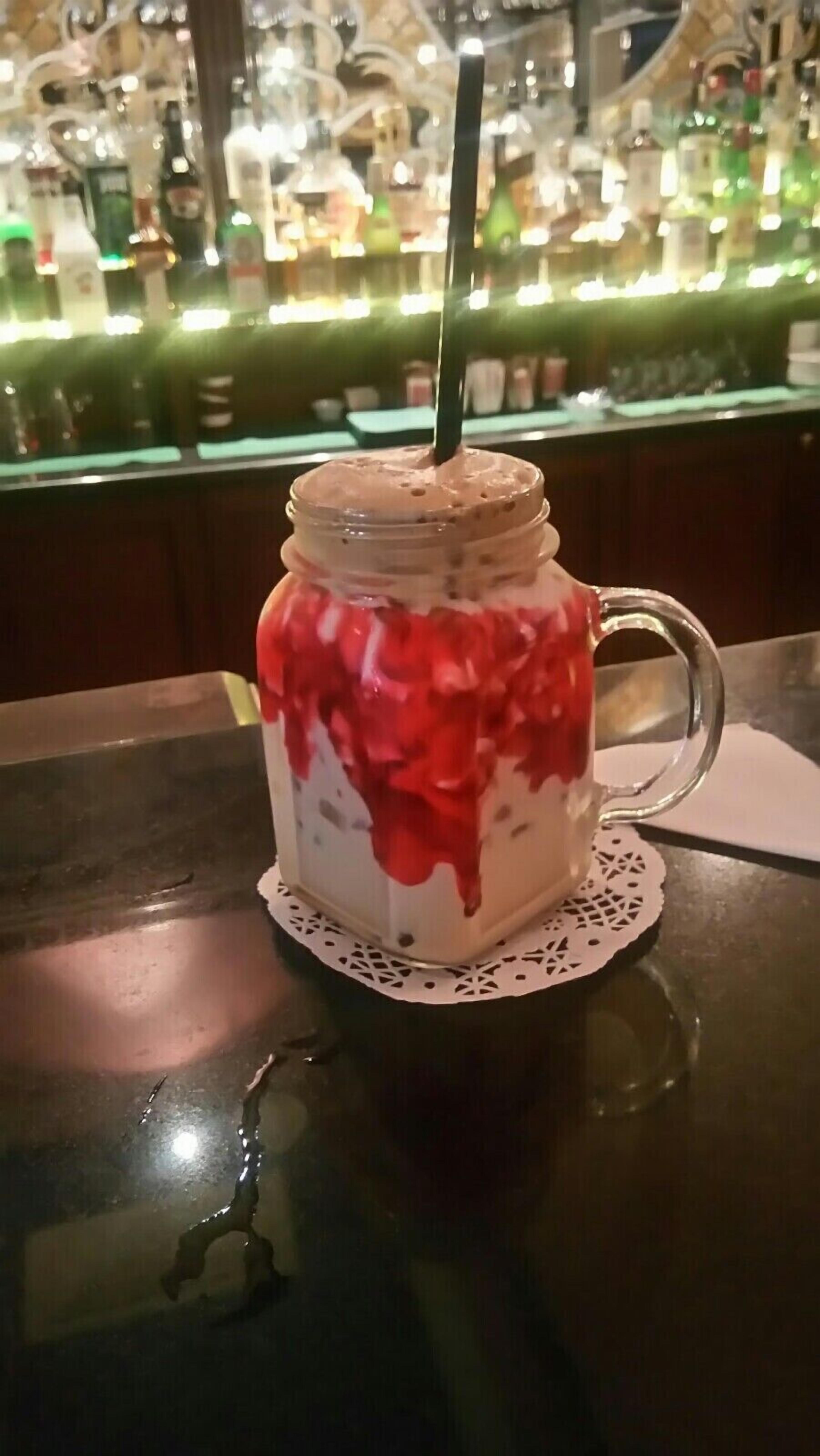 A glass jar with a handle filled with a layered beverage, a straw, and a doily on a table.