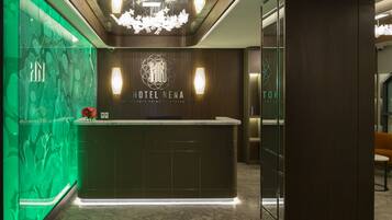 A modern hotel reception area with a marble counter, a chandelier, and a green wall with abstract patterns.