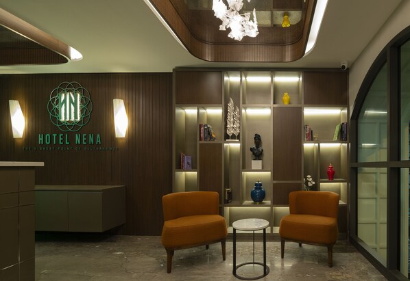 Un vestíbulo de hotel moderno con mostrador de recepción, dos sillones, una mesita y una pared decorativa con estanterías.