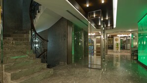 Eine moderne Lobby mit einer Marmortreppe, einem Glastür-Eingang und einer grüne Wand.