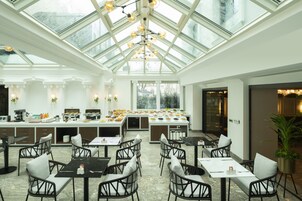 Un restaurante luminoso y espacioso con techo alto y ventanas grandes. Mesas y sillas dispuestas para comer.