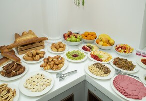 Un tavolo da buffet con diversi cibi, tra cui pane, dolci, frutta e verdura.