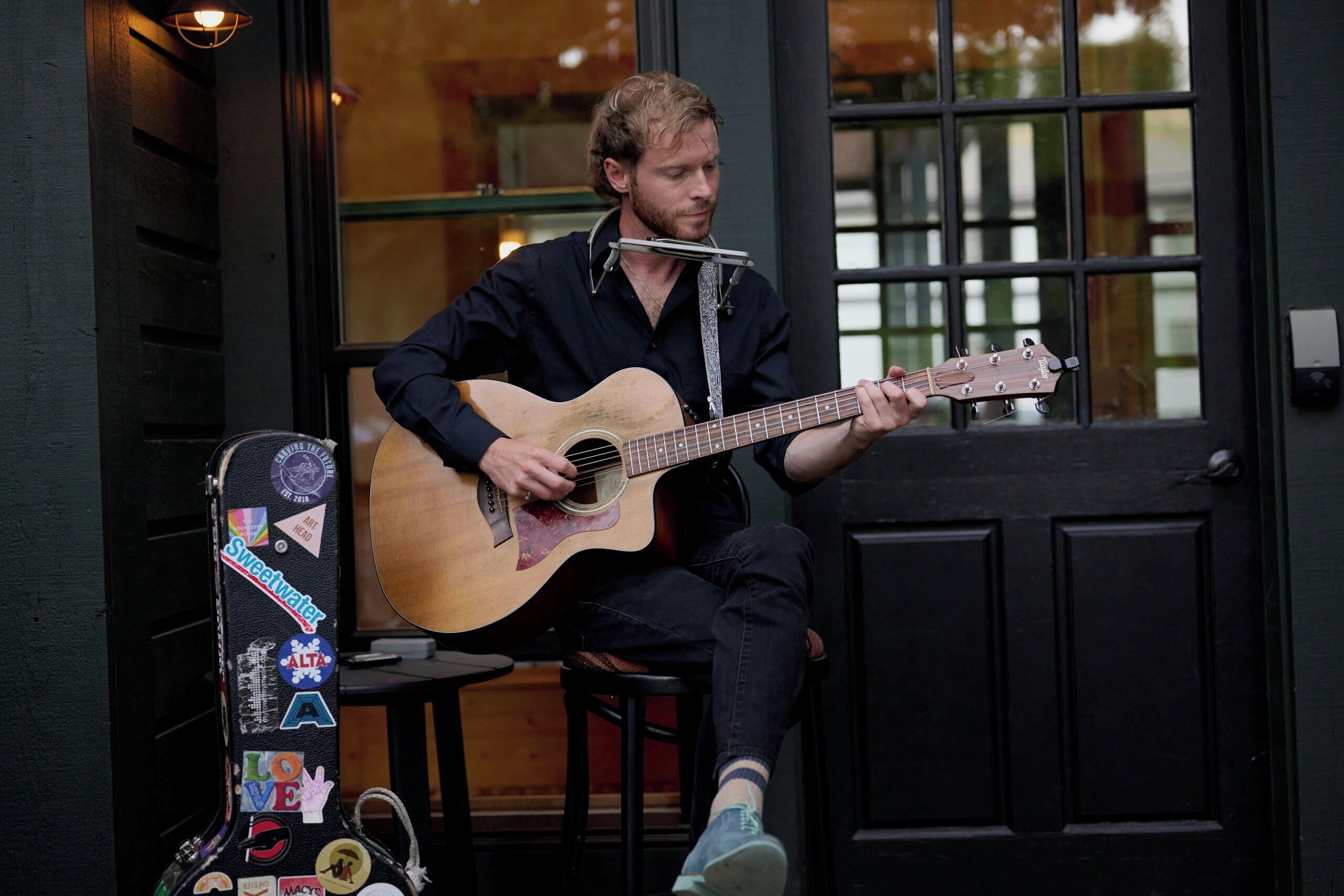 A person seated on a chair playing an acoustic guitar.