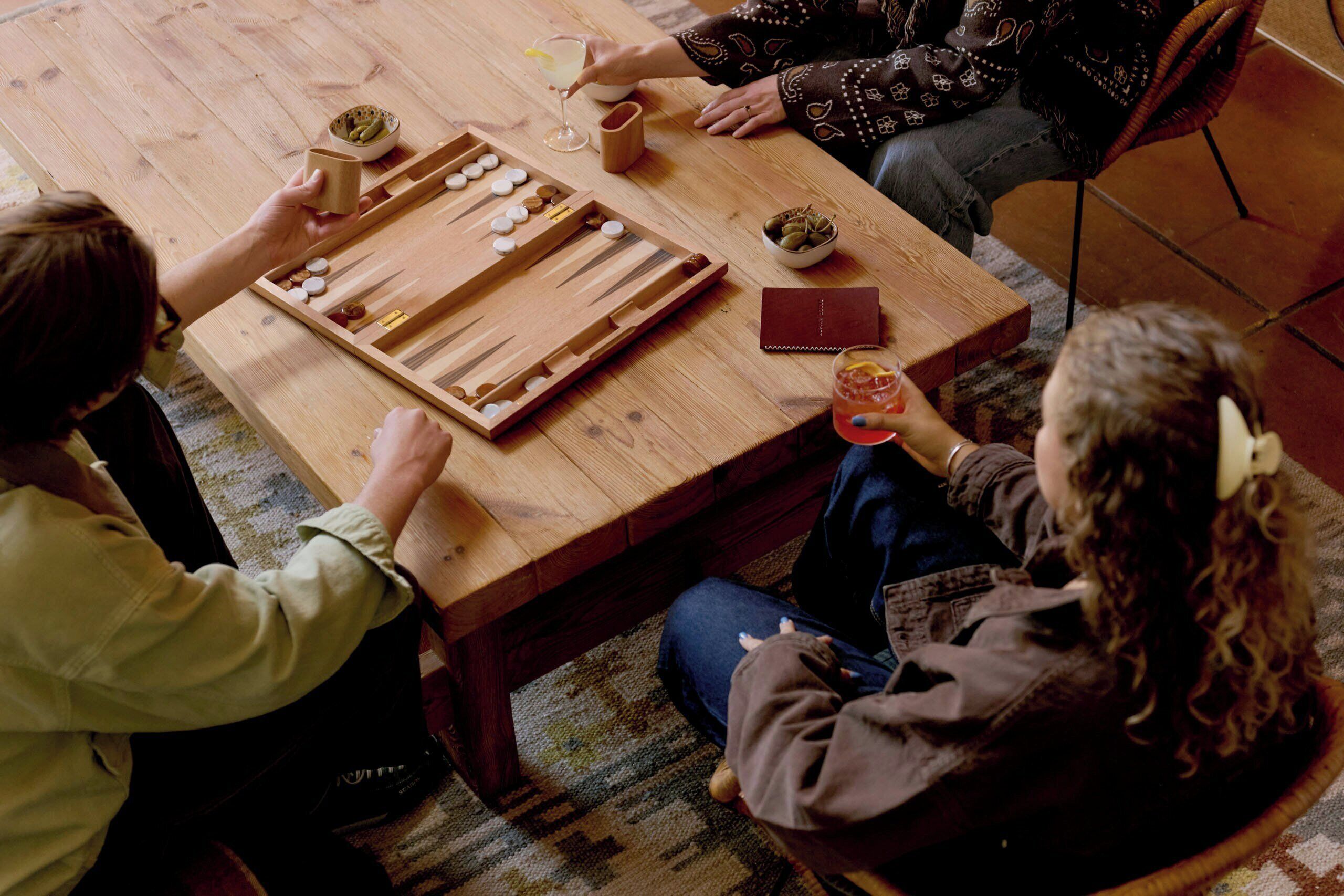 A group of people playing a board game at a wooden table with snacks and drinks.