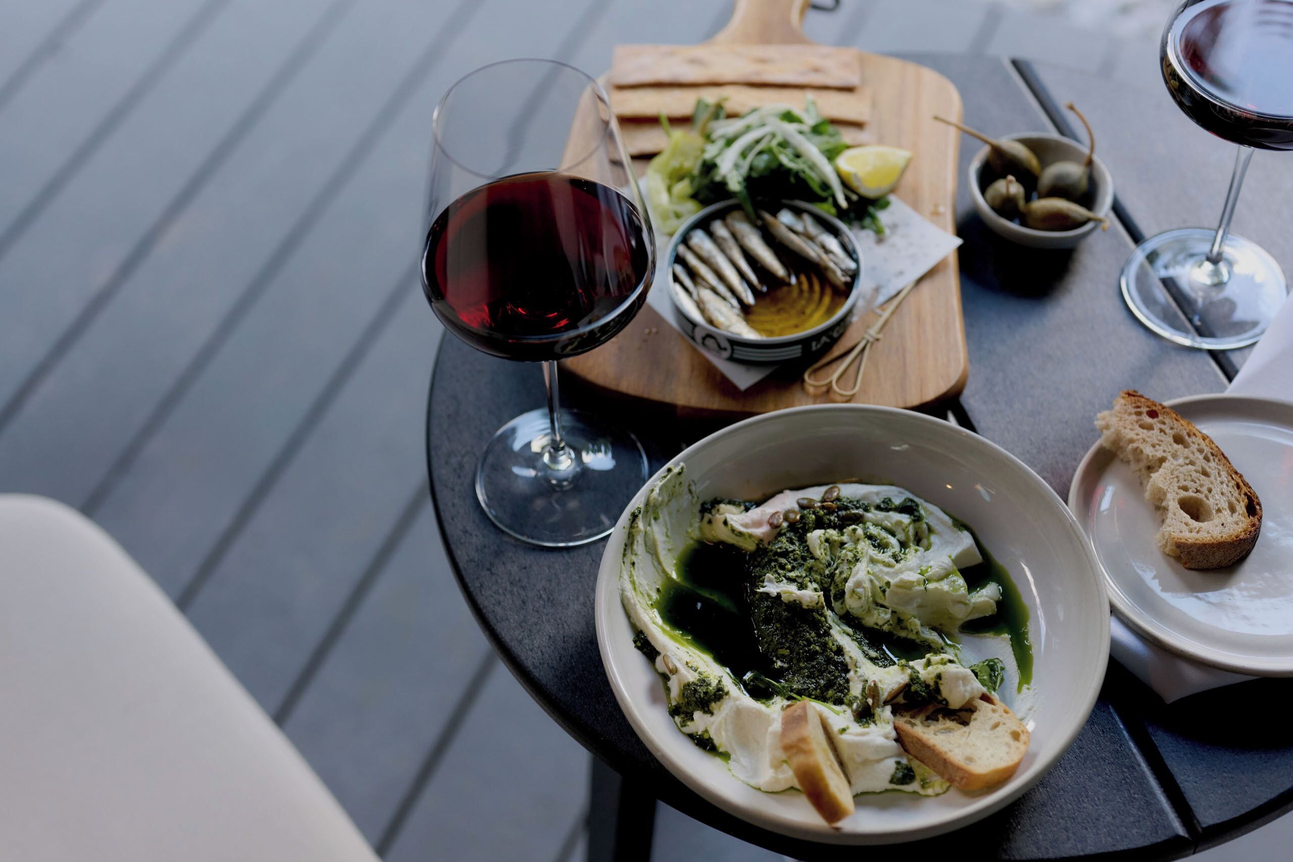 A dining table with a bowl of food, a plate of bread, and two glasses of red wine.